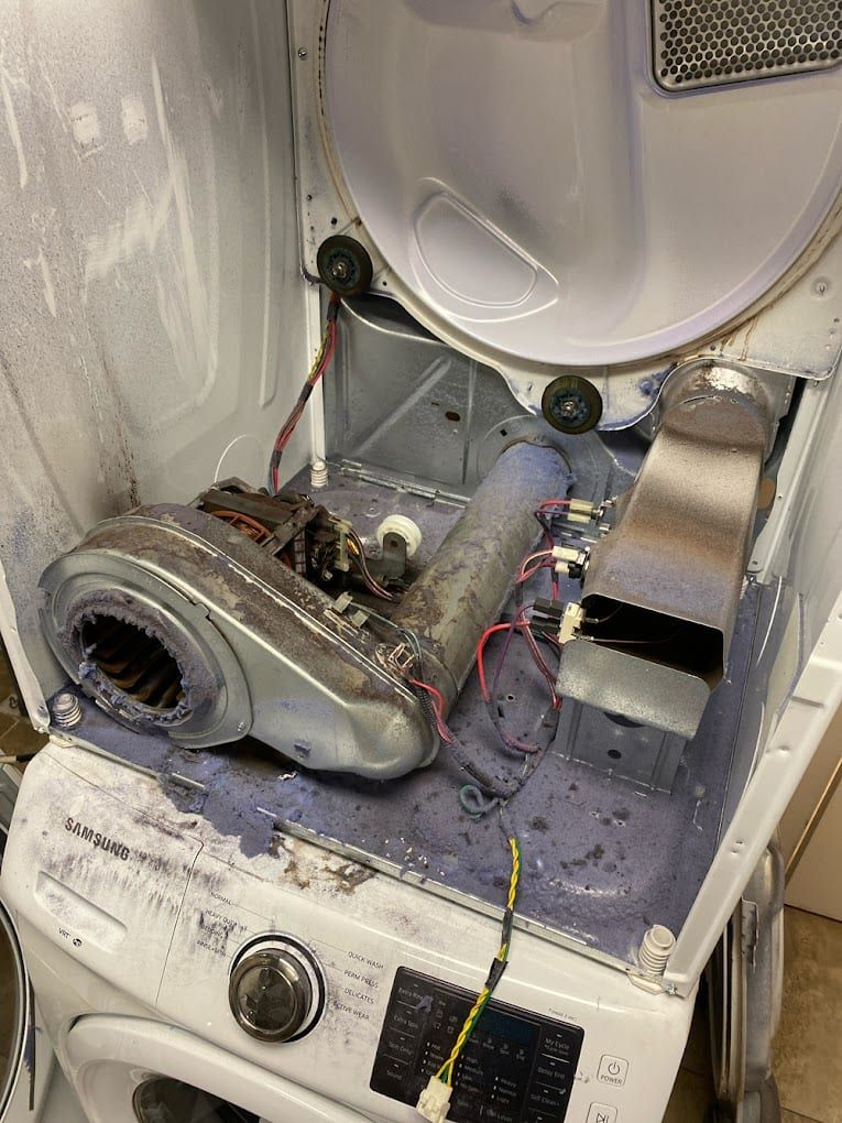 Dryer repair in Toronto — opened dryer showing the blower housing, tubular heating element and thermostats under a thick layer of lint