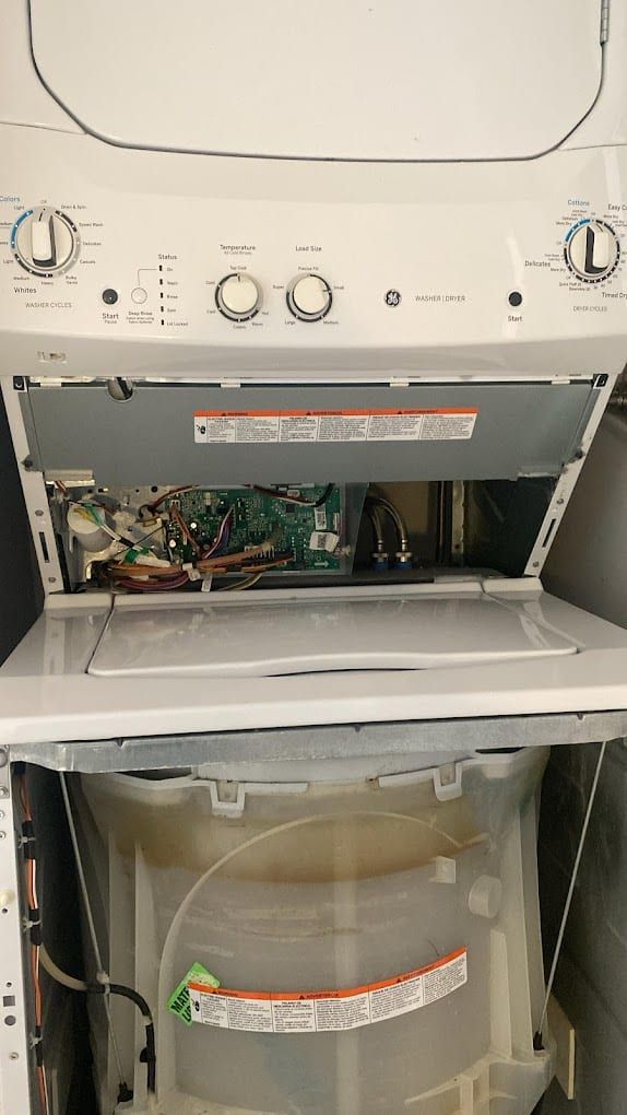 GE washer repair in Toronto — stacked GE washer and dryer with the control console folded down, exposing the main board, wiring harness and inlet valves